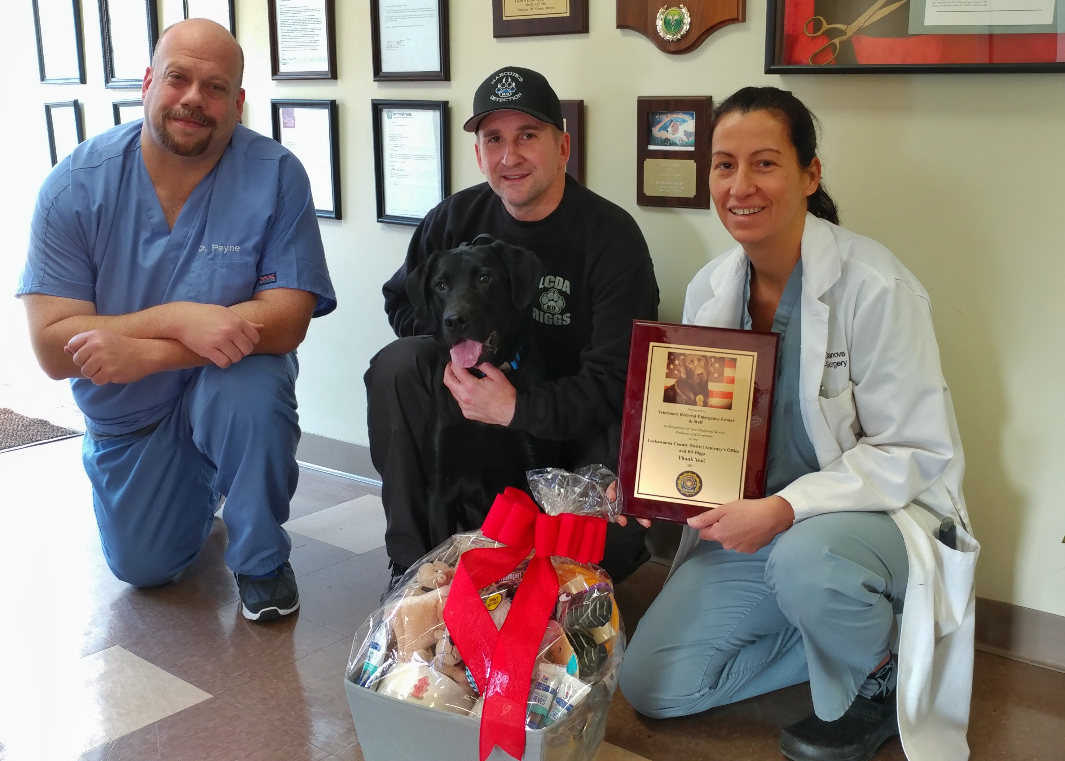 Doctors, trained dog, and handler pose with award and gift basket